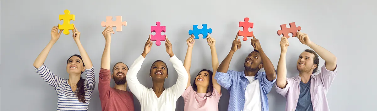 A diverse team holding up colorful jigsaw-puzzle pieces, looking up at them together.